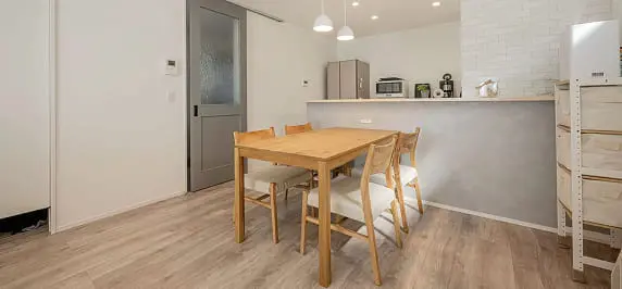 木製のテーブルとチェアが配置されたダイニングスペース。グレーの腰壁とペンダントライトが洗練された印象を与える