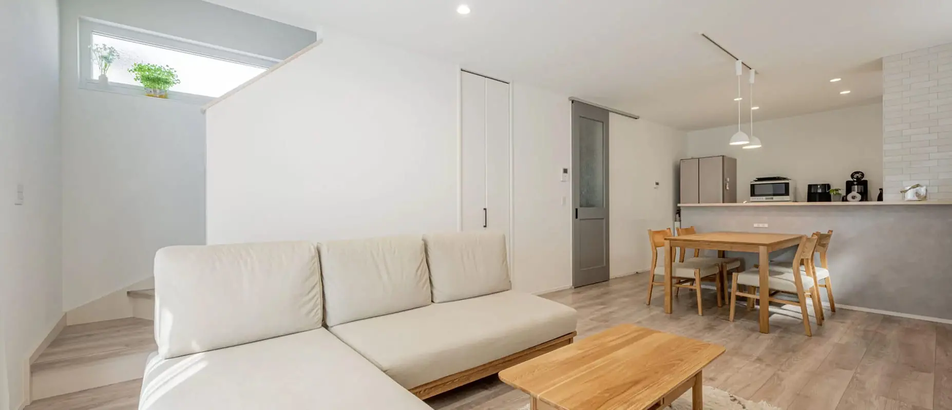 明るく開放的なリビング・ダイニング。白を基調とした壁と天井に、ナチュラルウッドの家具とグレーのアクセントドアが調和したシンプルモダンな空間。