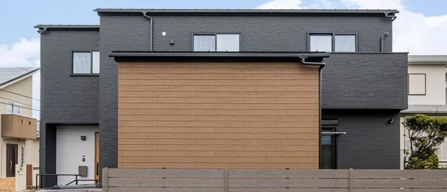 黒と木目調の外壁が印象的な、モダンデザインの二階建て住宅。直線的でシャープな外観に、プライバシーを意識した閉じたファサードが特徴。