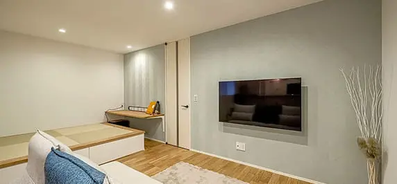 壁掛けテレビと隣接する小上がりの和室があるリビングスペース。奥には造作デスクがあり、作業や読書ができる落ち着いた空間が広がる。