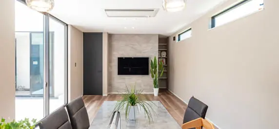 中庭に面した大きな窓から光が差し込む、明るくスタイリッシュなリビング。グレーのアクセント壁に設置されたテレビや観葉植物が洗練された印象を演出している。