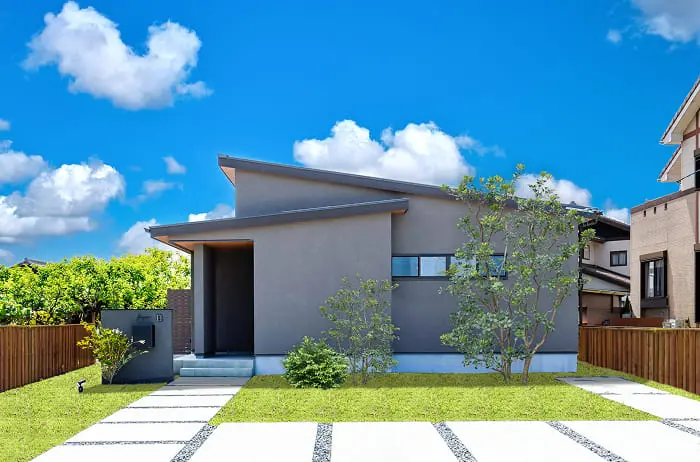シンプルでスタイリッシュな平屋住宅。グレーの外壁と片流れ屋根が特徴的で、手入れされた庭木がモダンな雰囲気を演出している。