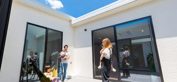 中庭スペースでリラックスする家族の様子。白い外壁に囲まれた開放的なプライベート空間で、子どもがハンモックに座り、両親が談笑する微笑ましいシーン。