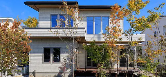 ナチュラルな雰囲気の二階建て住宅。レンガ調の外壁と木々に囲まれた庭が、自然と調和した優しい印象を与える。