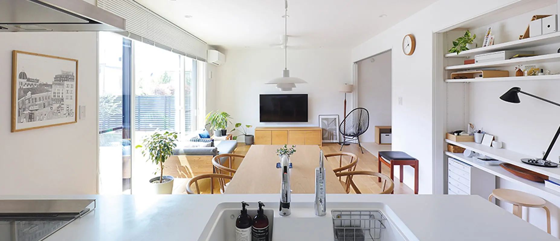 白を基調とした開放感のあるリビングダイニング。大きな窓から自然光が差し込み、観葉植物や木製家具が温もりを演出している。奥にはデスクスペースや壁付け収納も備わる。