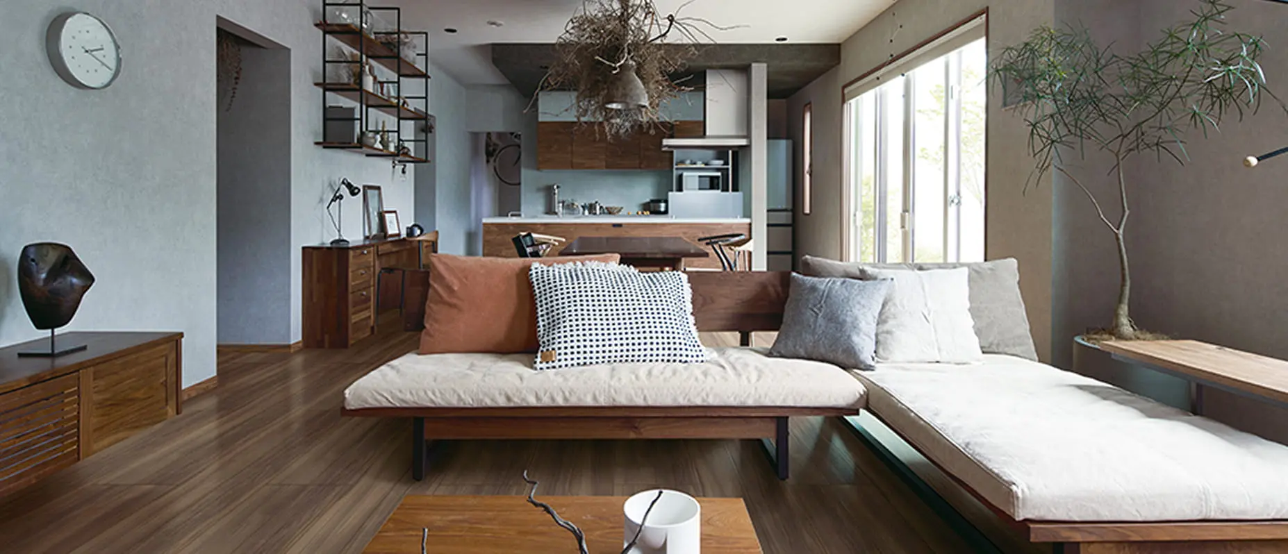 落ち着いたトーンで統一されたリビングダイニング。木製家具とグレーの壁が調和し、ドライフラワーの照明や観葉植物が自然の温もりを演出しているモダンな空間。