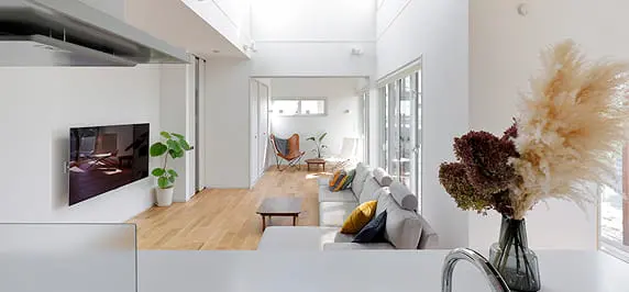 高い天井と大きな窓が開放感を生む、シンプルでモダンなリビング空間。白い壁と明るい木目の床が調和し、観葉植物やドライフラワーがアクセントに。