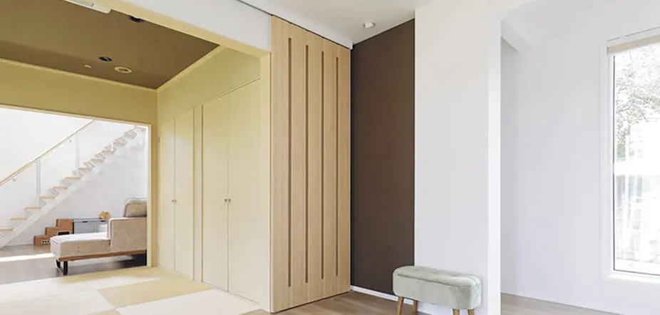 明るく開放感のある住宅の室内。左側には畳スペースと階段、右側には白い壁と大きな窓があり、ナチュラルな木の風合いが際立つデザイン。