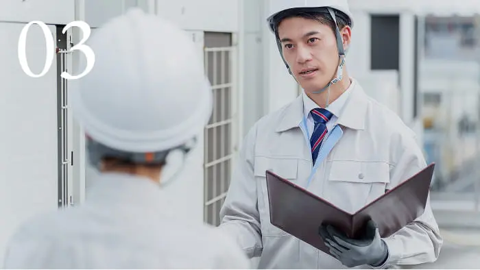 建設現場でヘルメットを着用した担当者が打ち合わせしている様子。安全確認や工事進捗の説明中。